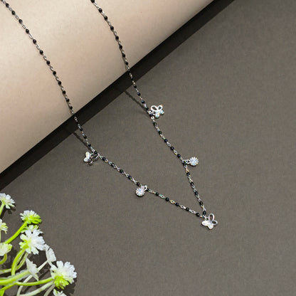 Silver necklace with floral pendants on a gray background with flowers.