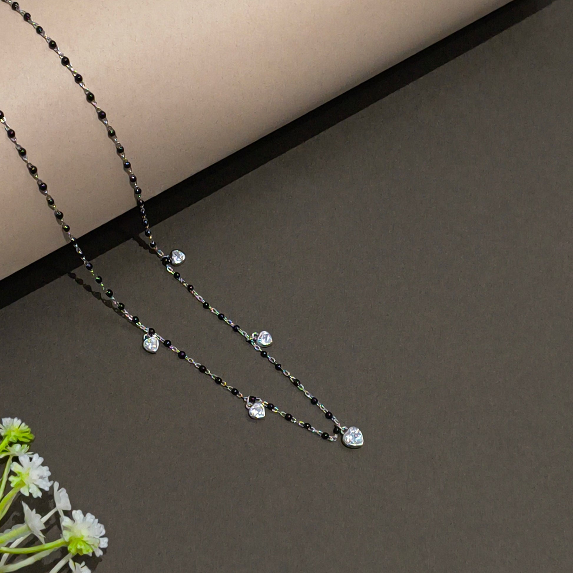 Necklace with black and clear beads on a gray surface with a white flower.