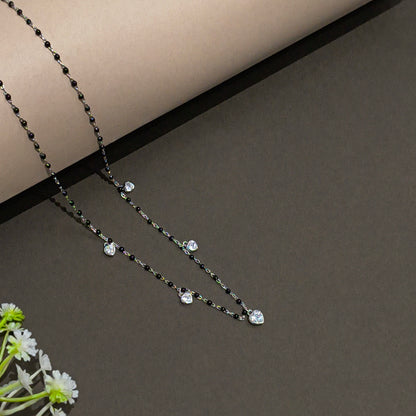 Necklace with black and clear beads on a gray surface with a white flower.