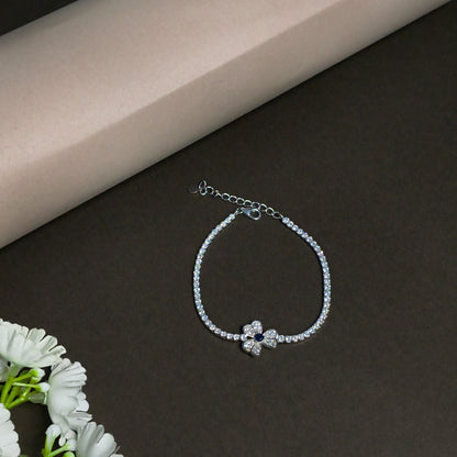Silver bracelet with a flower-shaped clasp on a dark surface with a beige corner and white flowers.