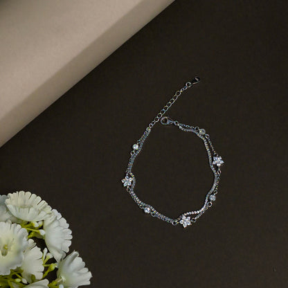 Silver bracelet with floral designs on a dark surface with white flowers.