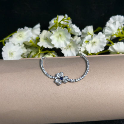 Silver bracelet with a floral design on a mannequin arm next to white flowers.