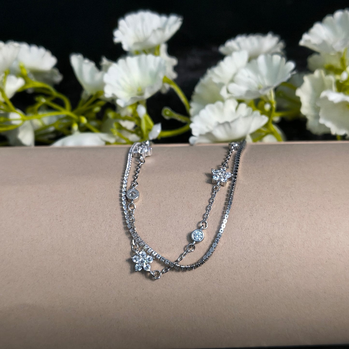 Silver bracelet on a mannequin arm with white flowers in the background