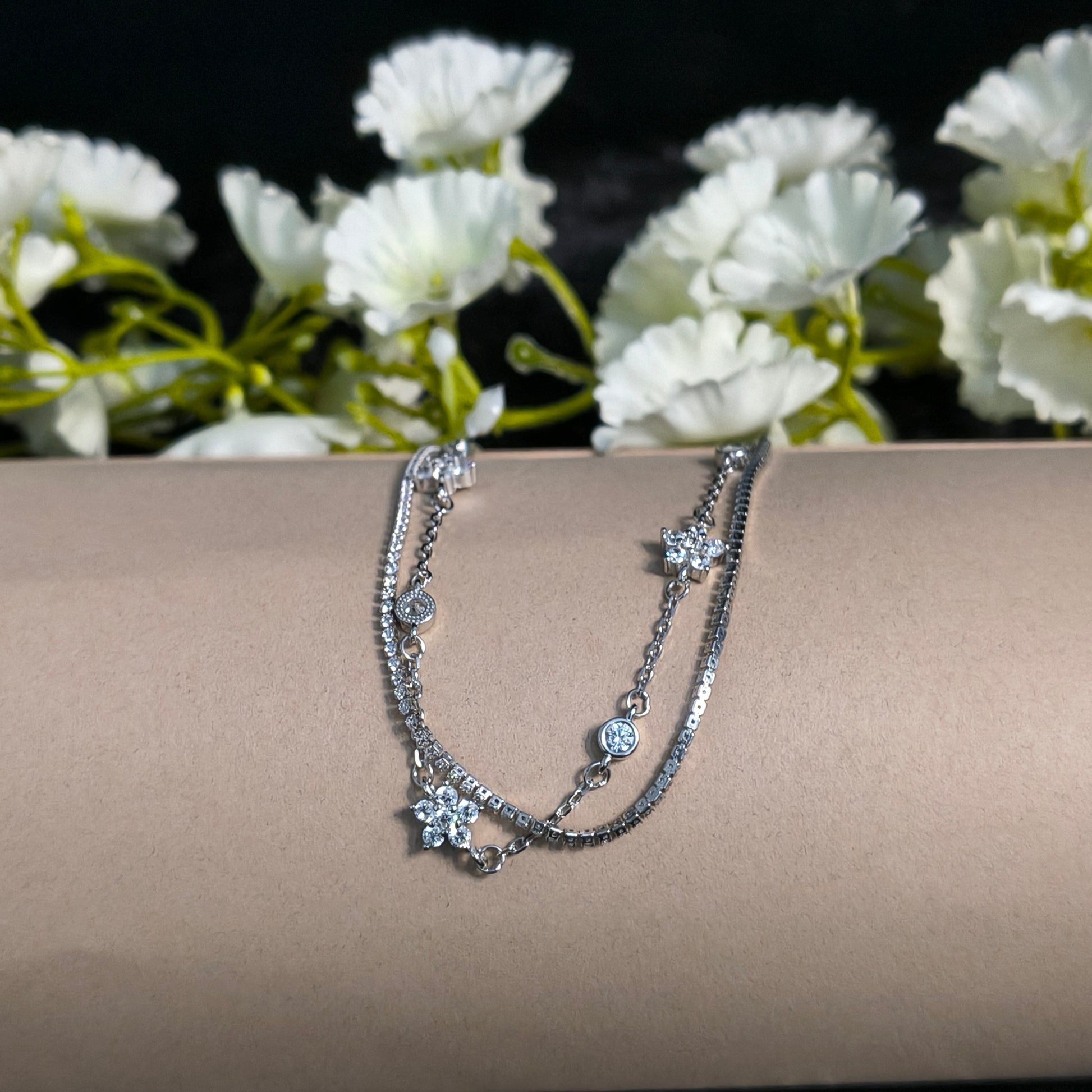 Silver bracelet on a mannequin arm with white flowers in the background