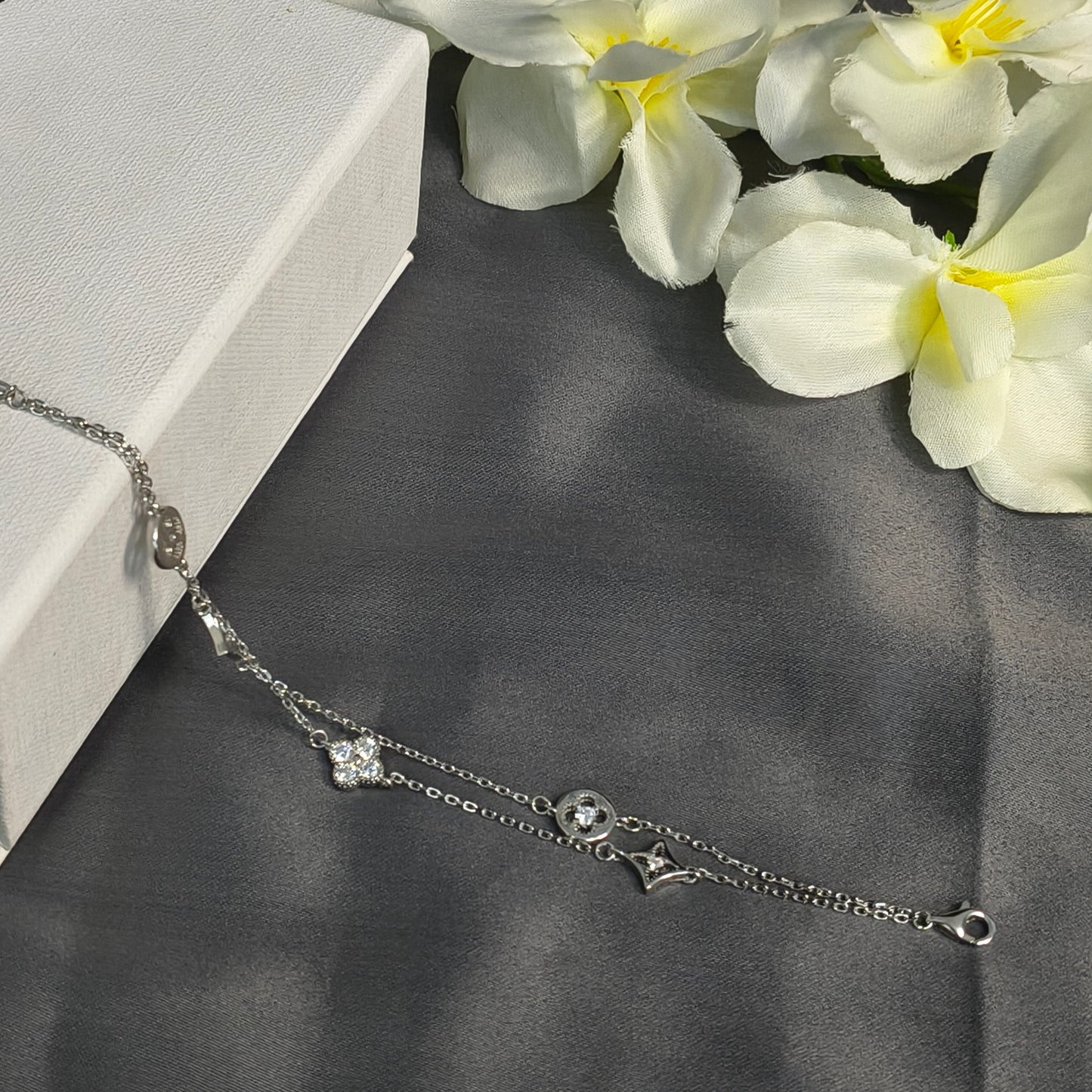Silver bracelet with floral design on a dark fabric background with white flowers.