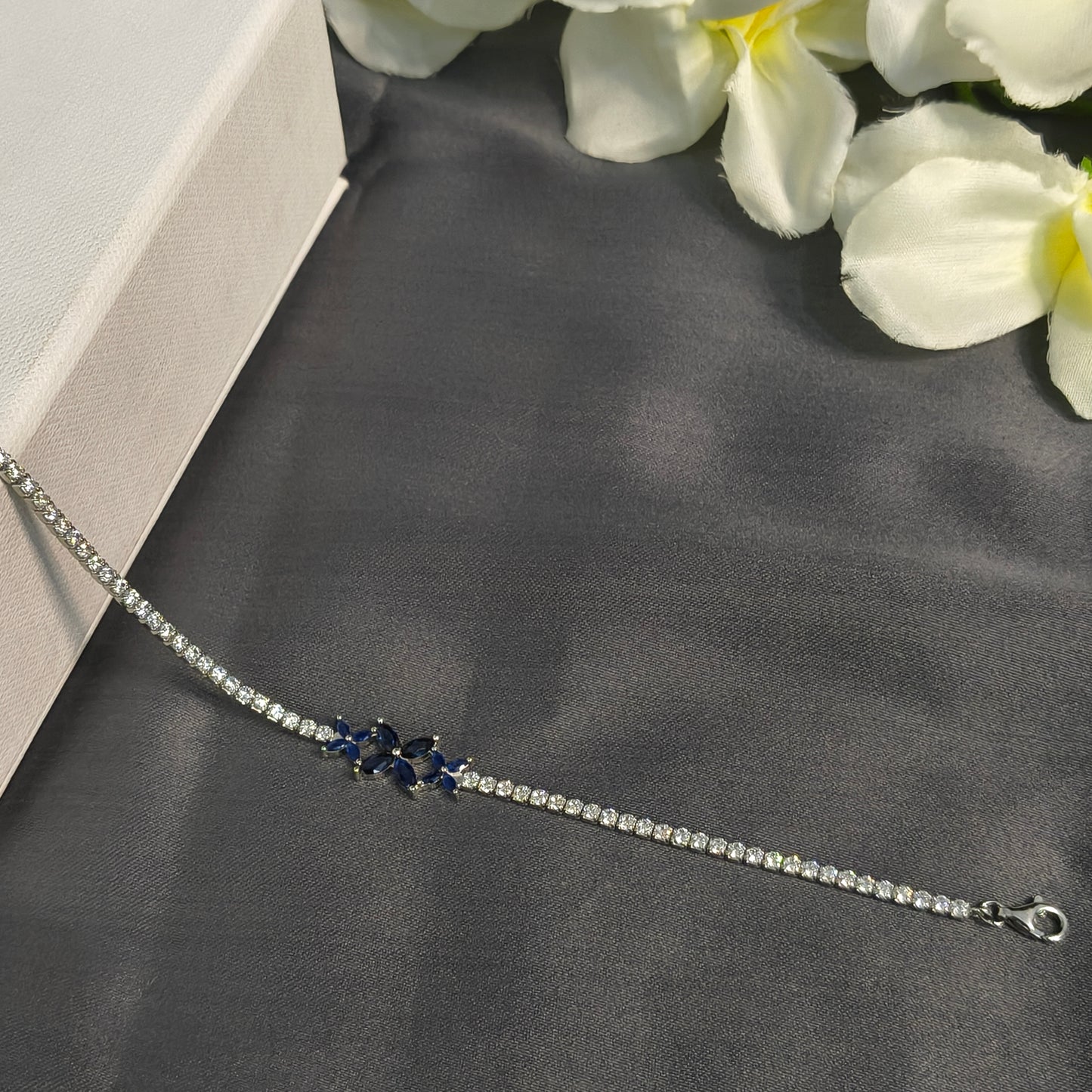 Silver bracelet with blue stones on a gray surface with white flowers