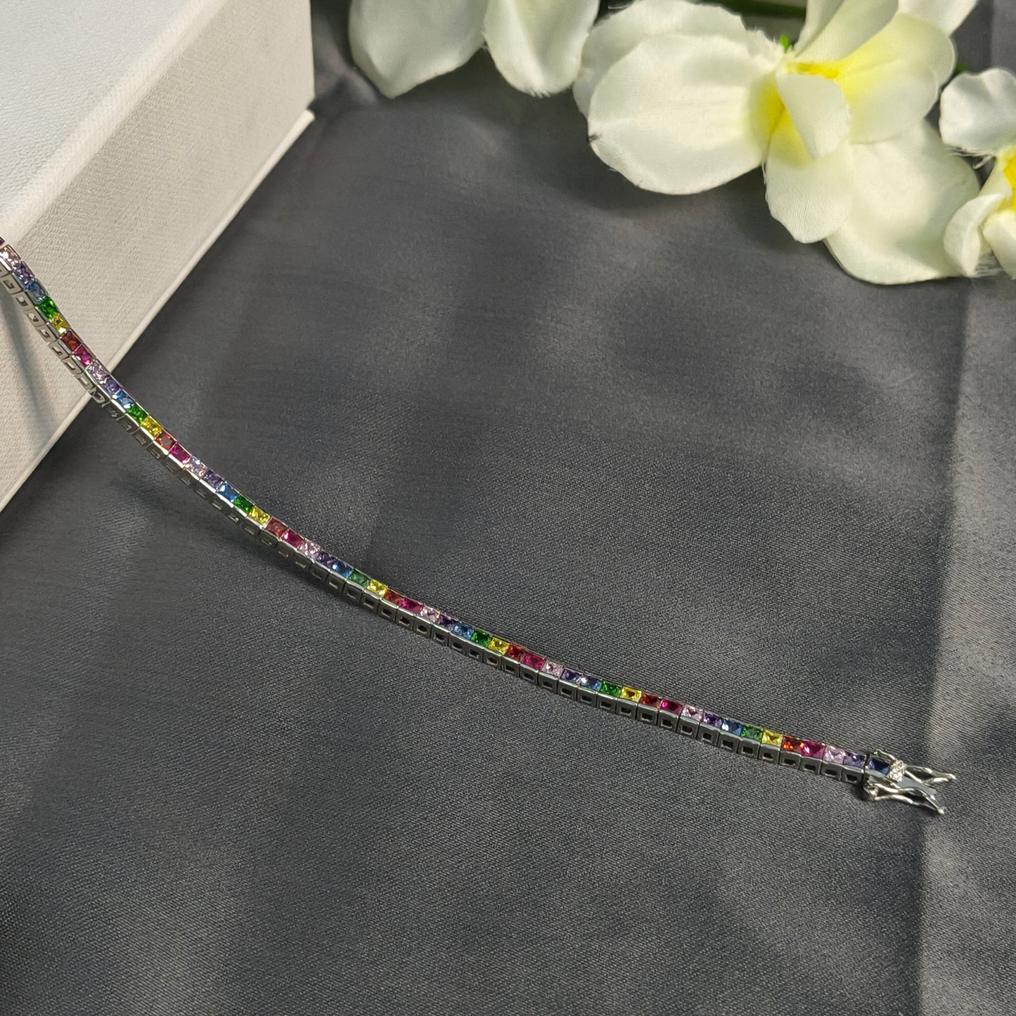 Multicolored gemstone bracelet on a dark fabric background with white flowers.