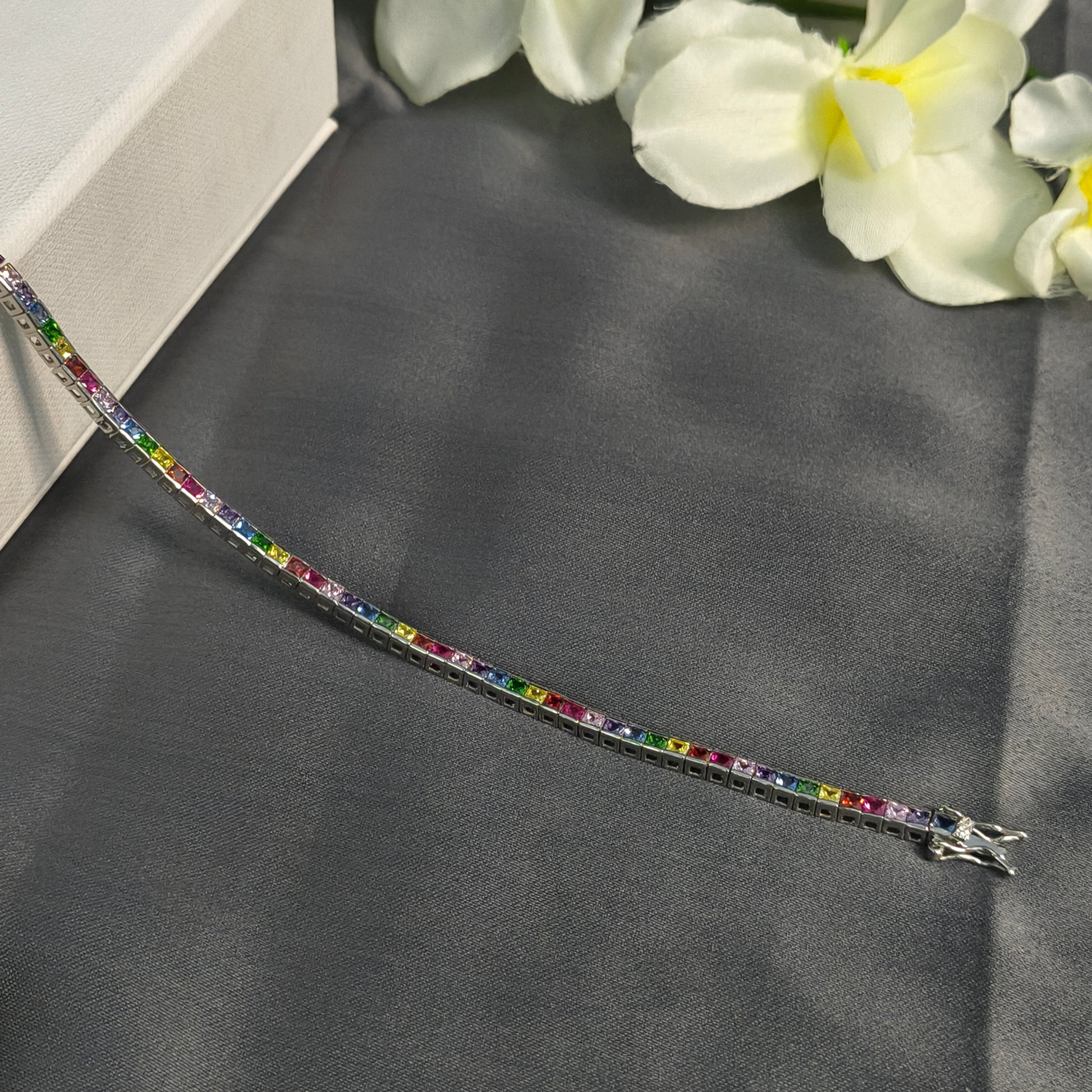 Multicolored gemstone bracelet on a dark fabric background with white flowers.