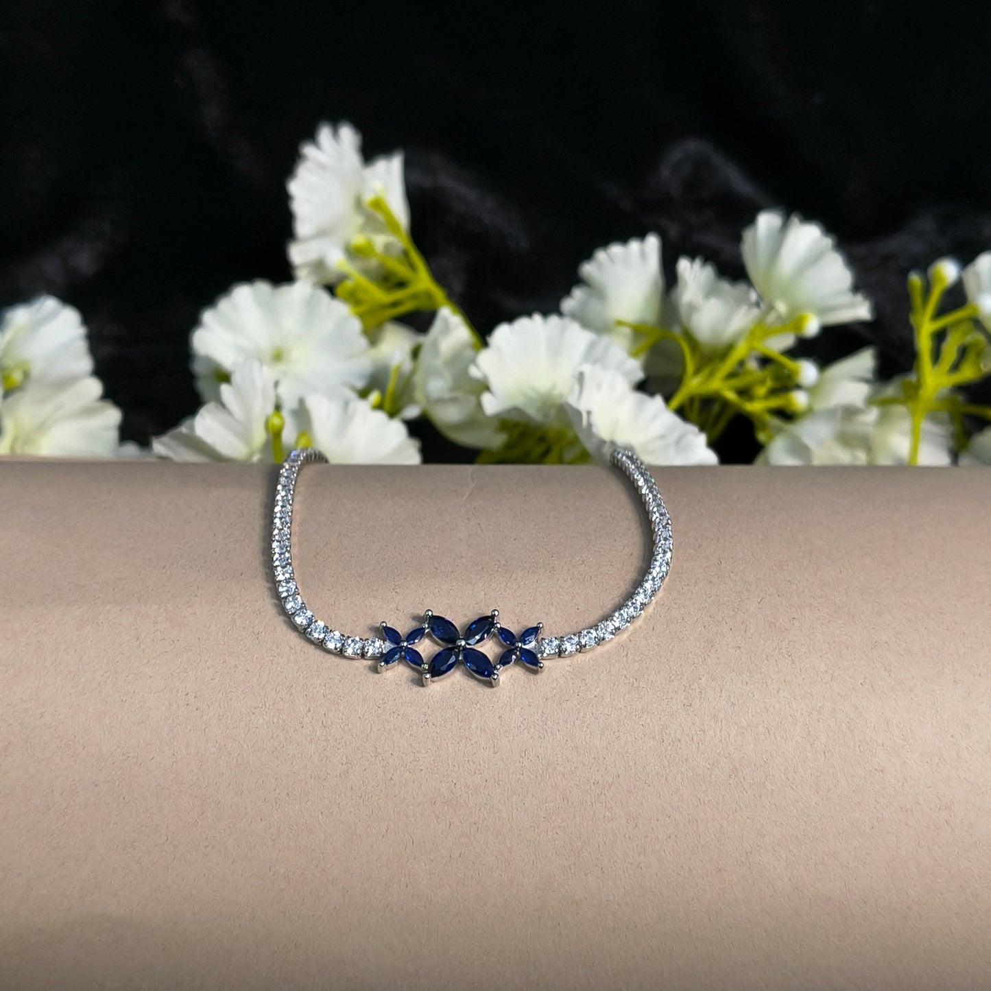 Silver hoop earring with blue gemstones on a beige stand with white flowers in the background