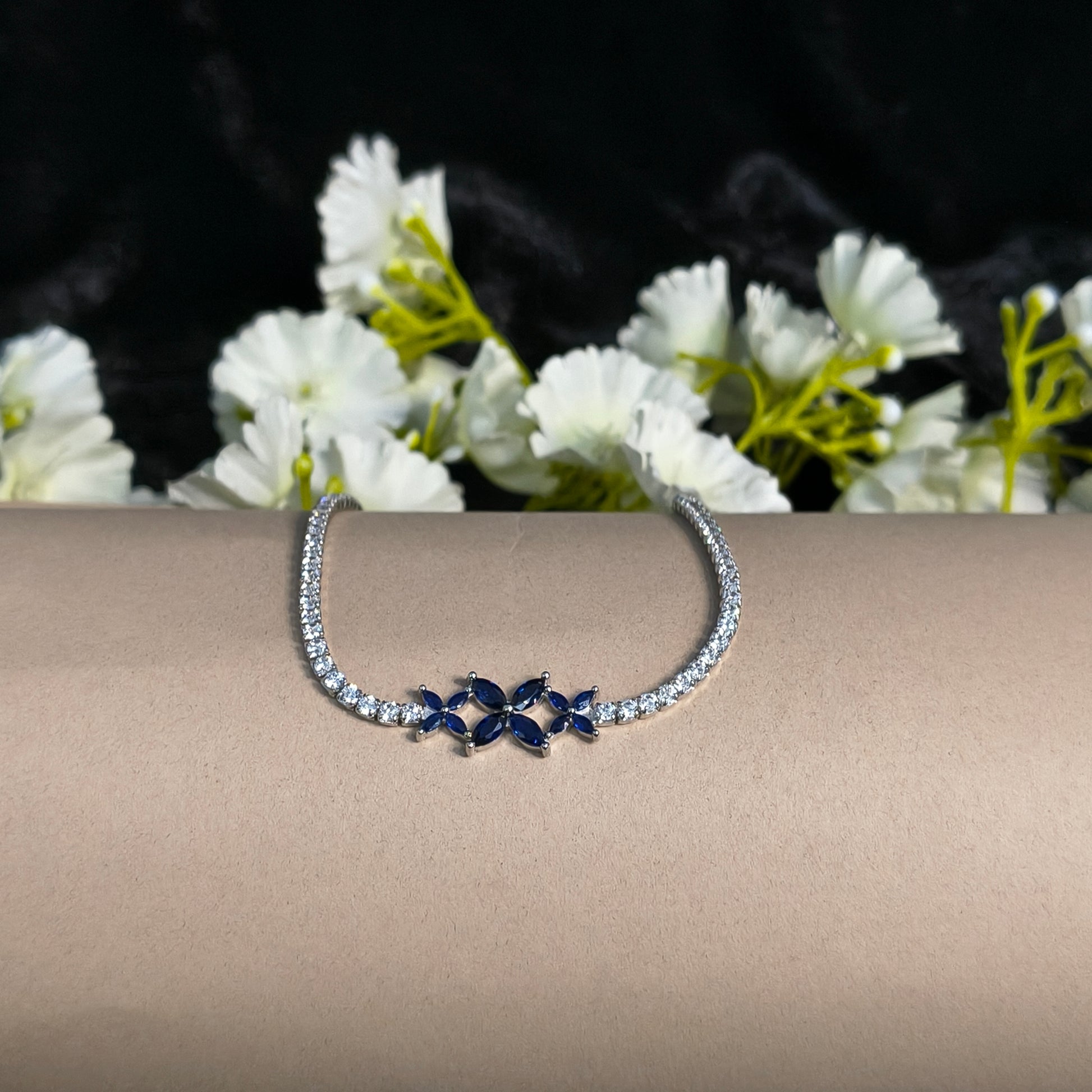 Silver hoop earring with blue gemstones on a beige stand with white flowers in the background