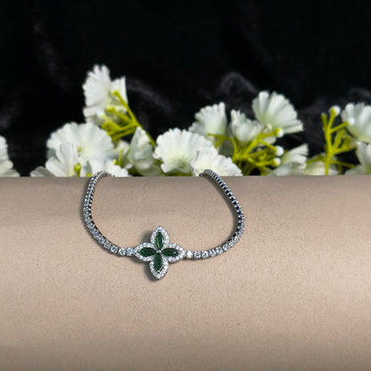Silver bracelet with green gemstone on a person's wrist, next to white flowers.