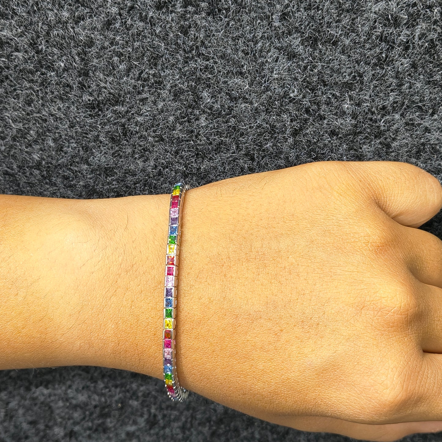 Multicolored beaded bracelet on a wrist against a gray background