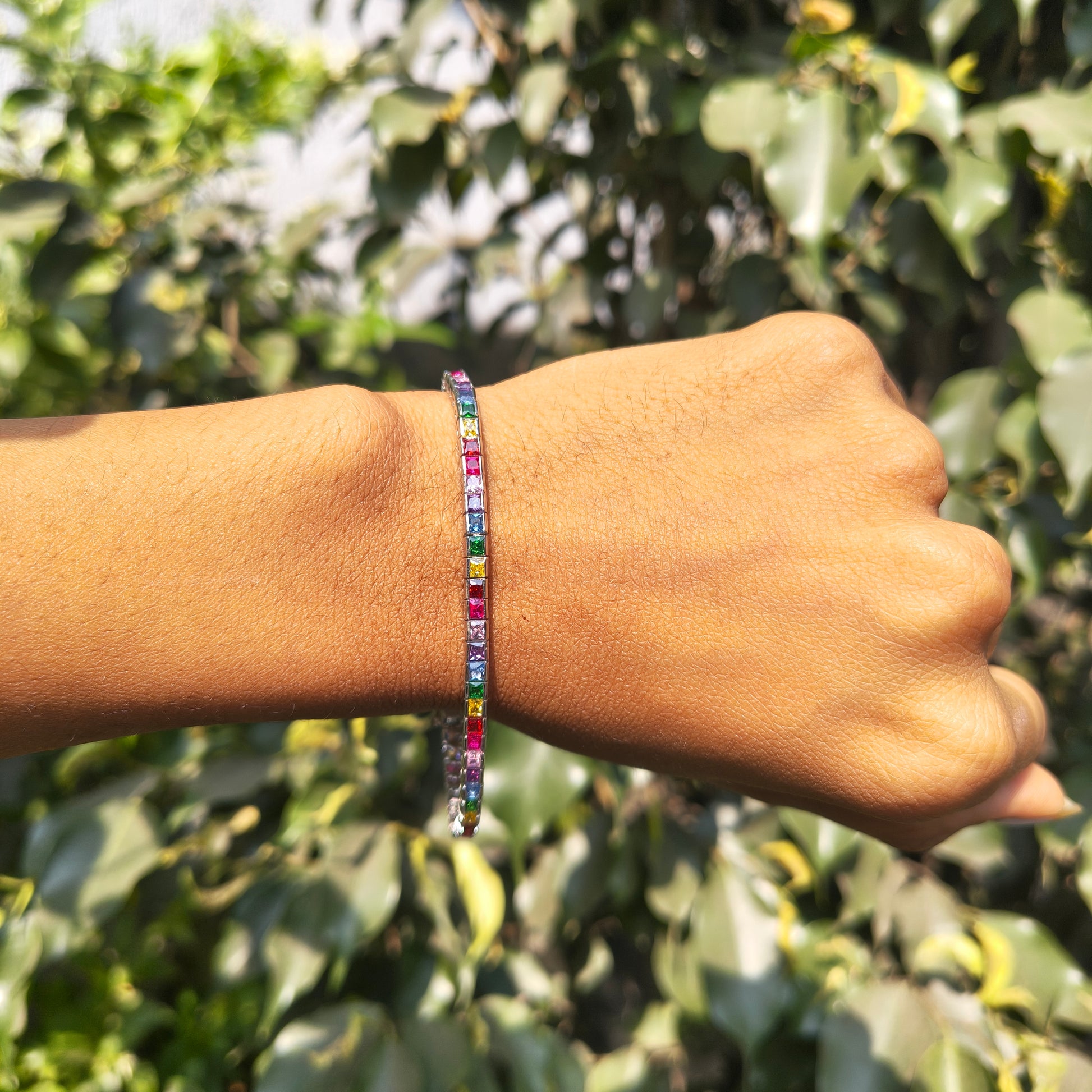 Hand wearing a colorful beaded bracelet with a green leafy background