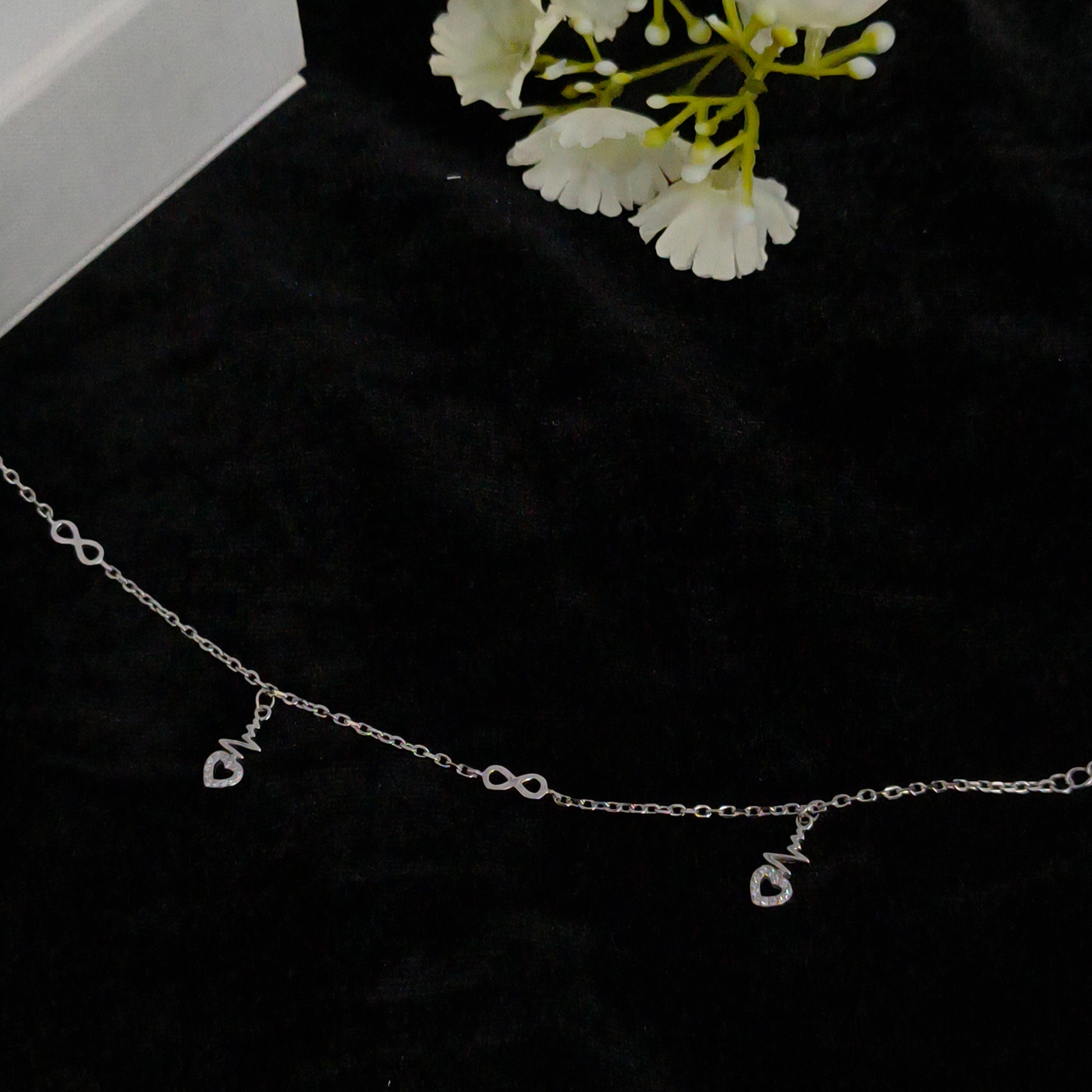 Silver chain necklace on a black background with white flowers