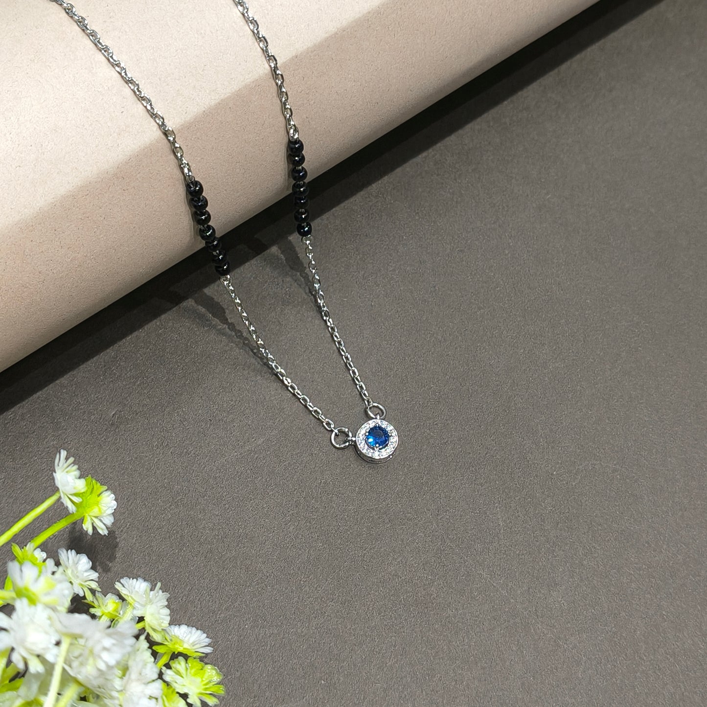Necklace with a blue gemstone on a gray surface with flowers in the corner