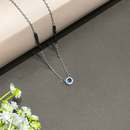 Necklace with a blue gemstone on a gray surface with flowers in the corner