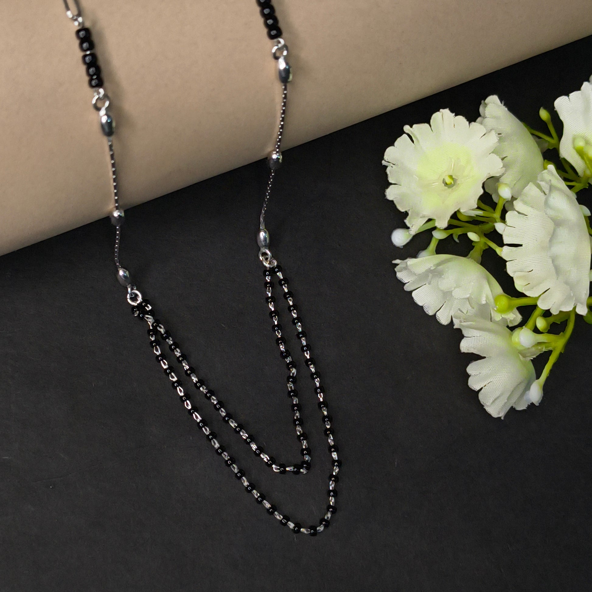Silver chain necklace on a dark surface with light-colored flowers.