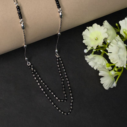 Silver chain necklace on a dark surface with light-colored flowers.