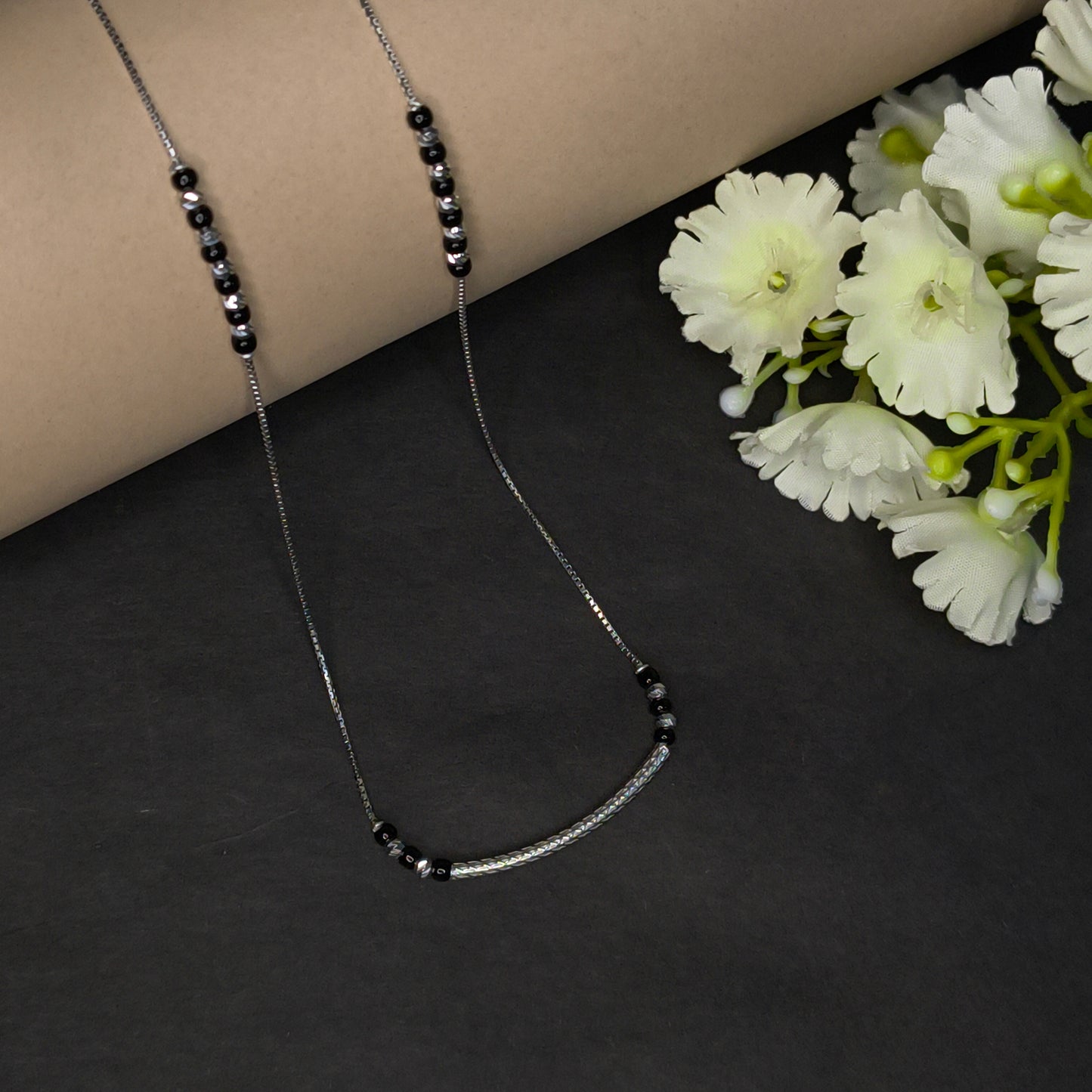 Necklace with black beads on a dark surface with white flowers