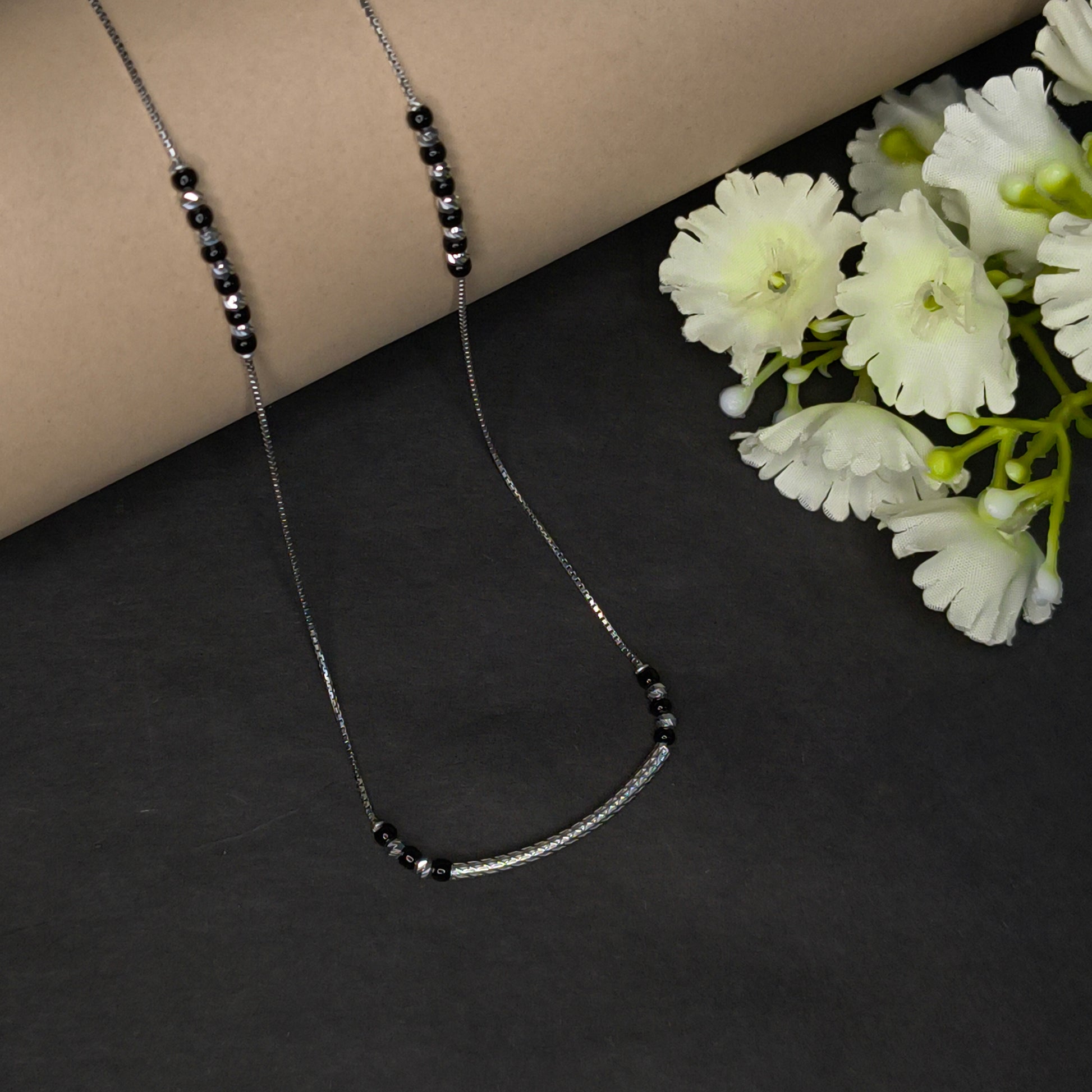 Necklace with black beads on a dark surface with white flowers