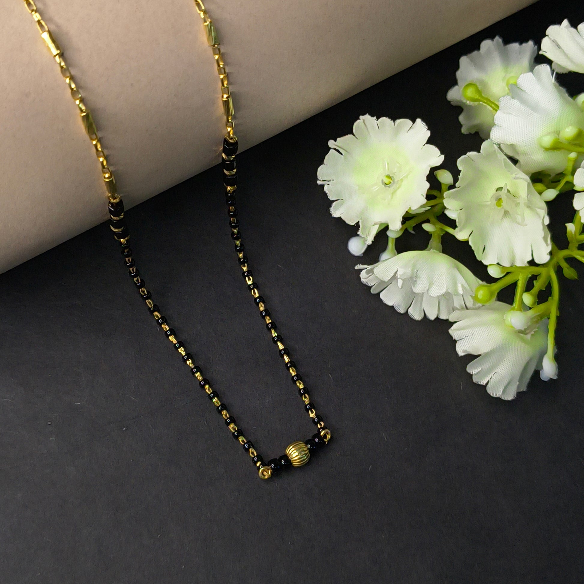 Gold chain necklace on a dark surface with white flowers