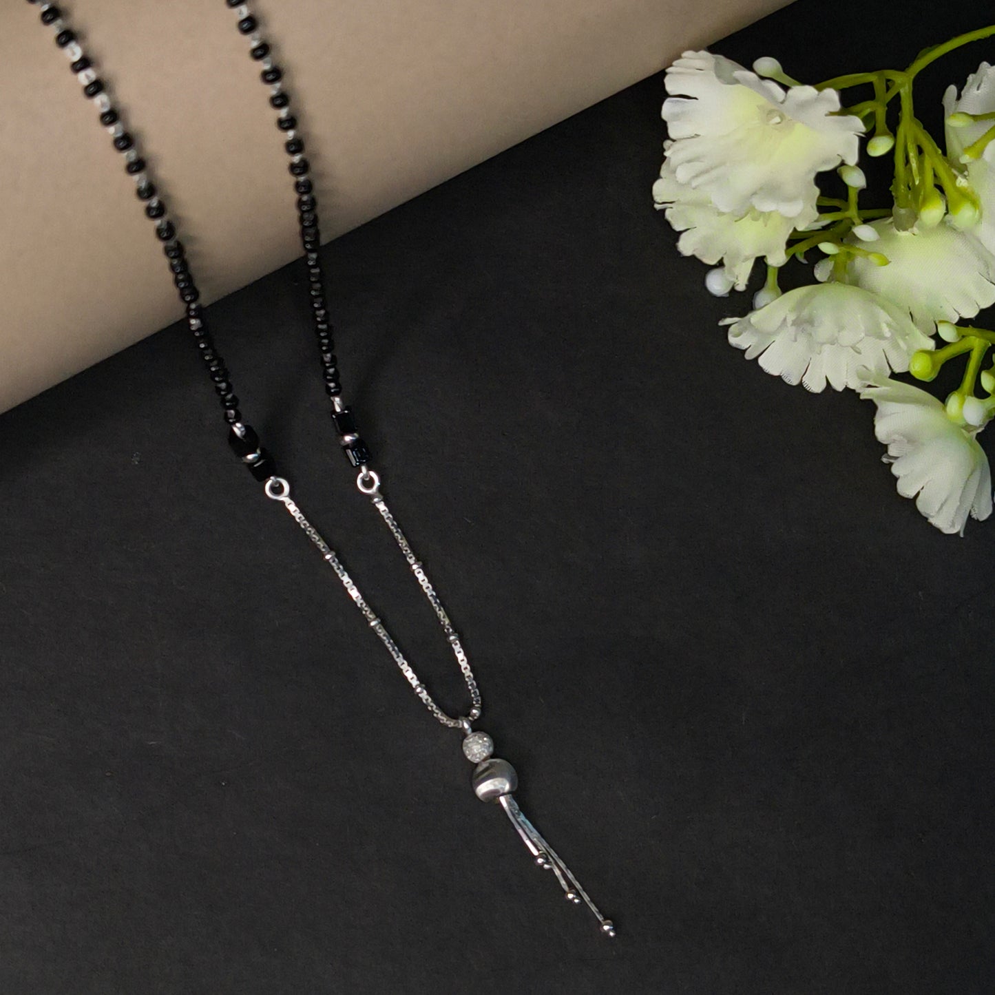 Two beaded necklaces on a dark surface with white flowers in the corner.
