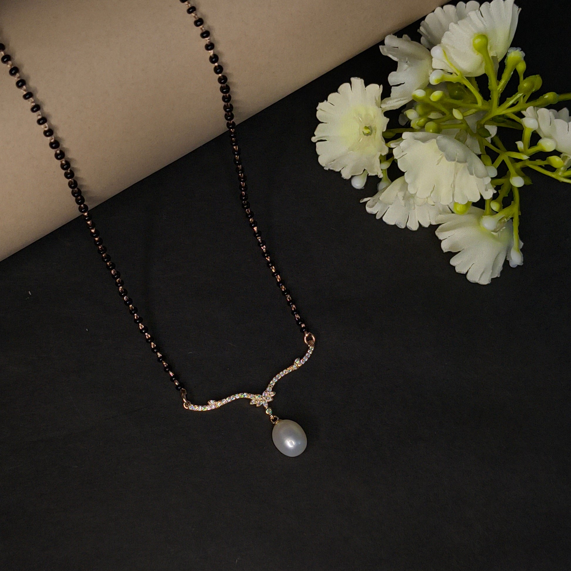 Necklace with a pearl pendant on a dark surface with white flowers.