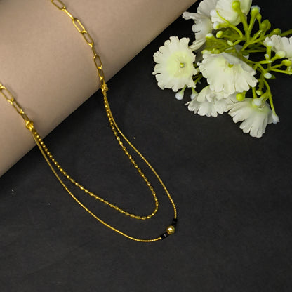 Gold chain necklace on a dark surface with white flowers