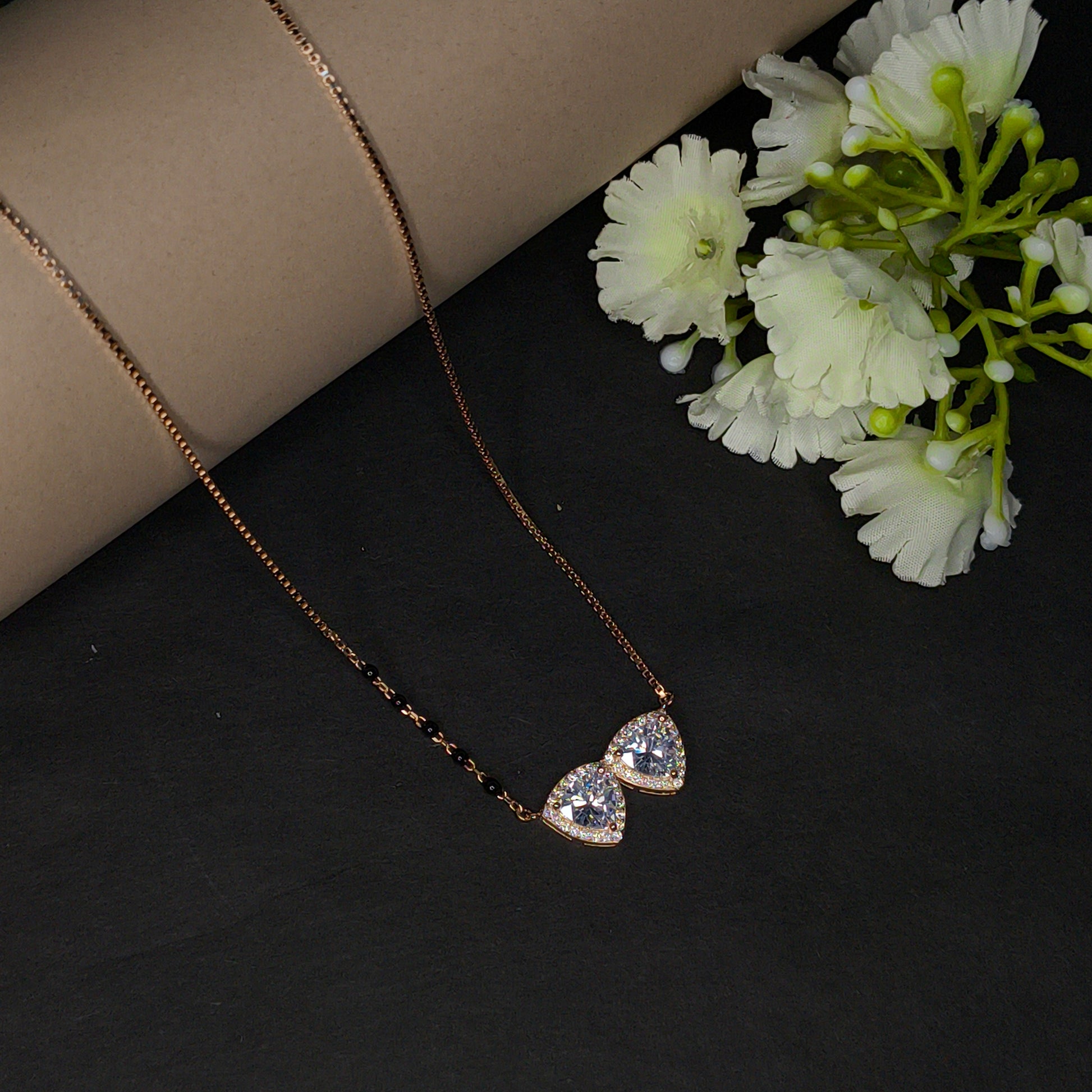 Gold necklace with heart-shaped pendants on a black surface with white flowers.