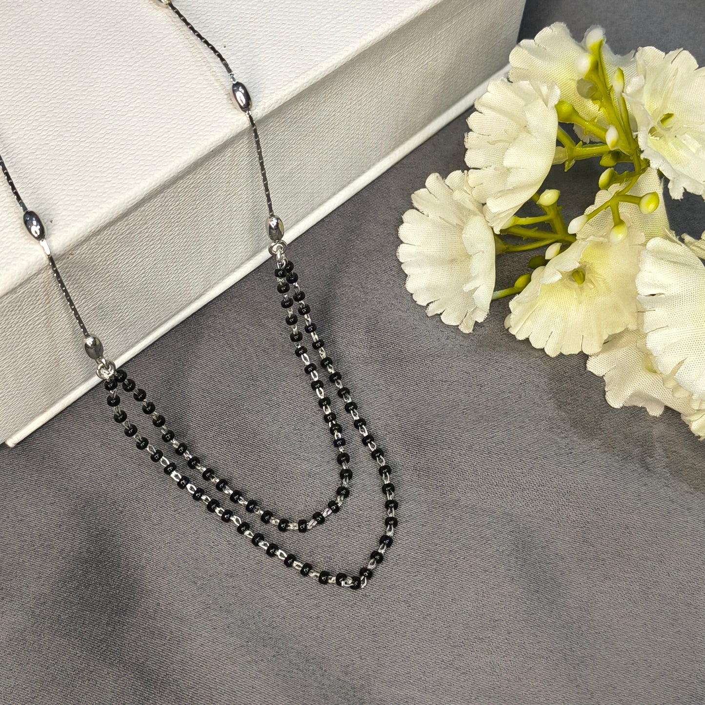 Black beaded necklace on a gray surface with white flowers