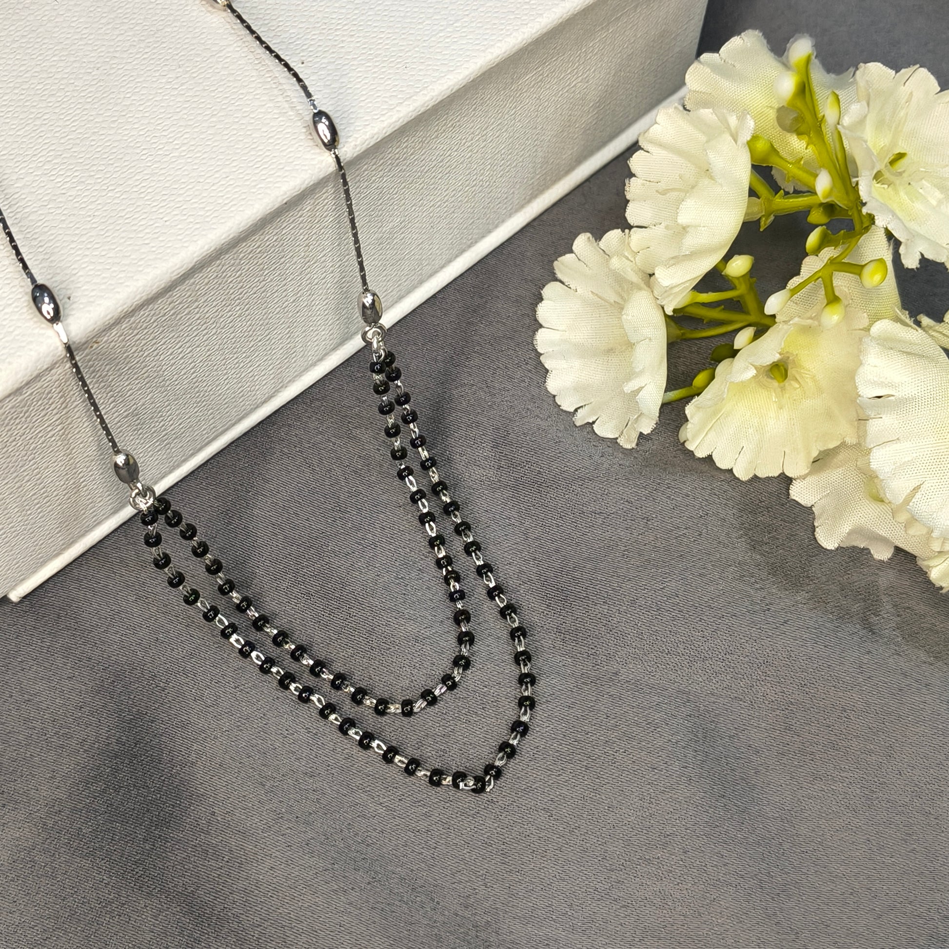Black beaded necklace on a gray surface with white flowers