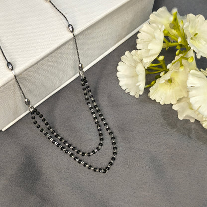 Black beaded necklace on a gray surface with white flowers