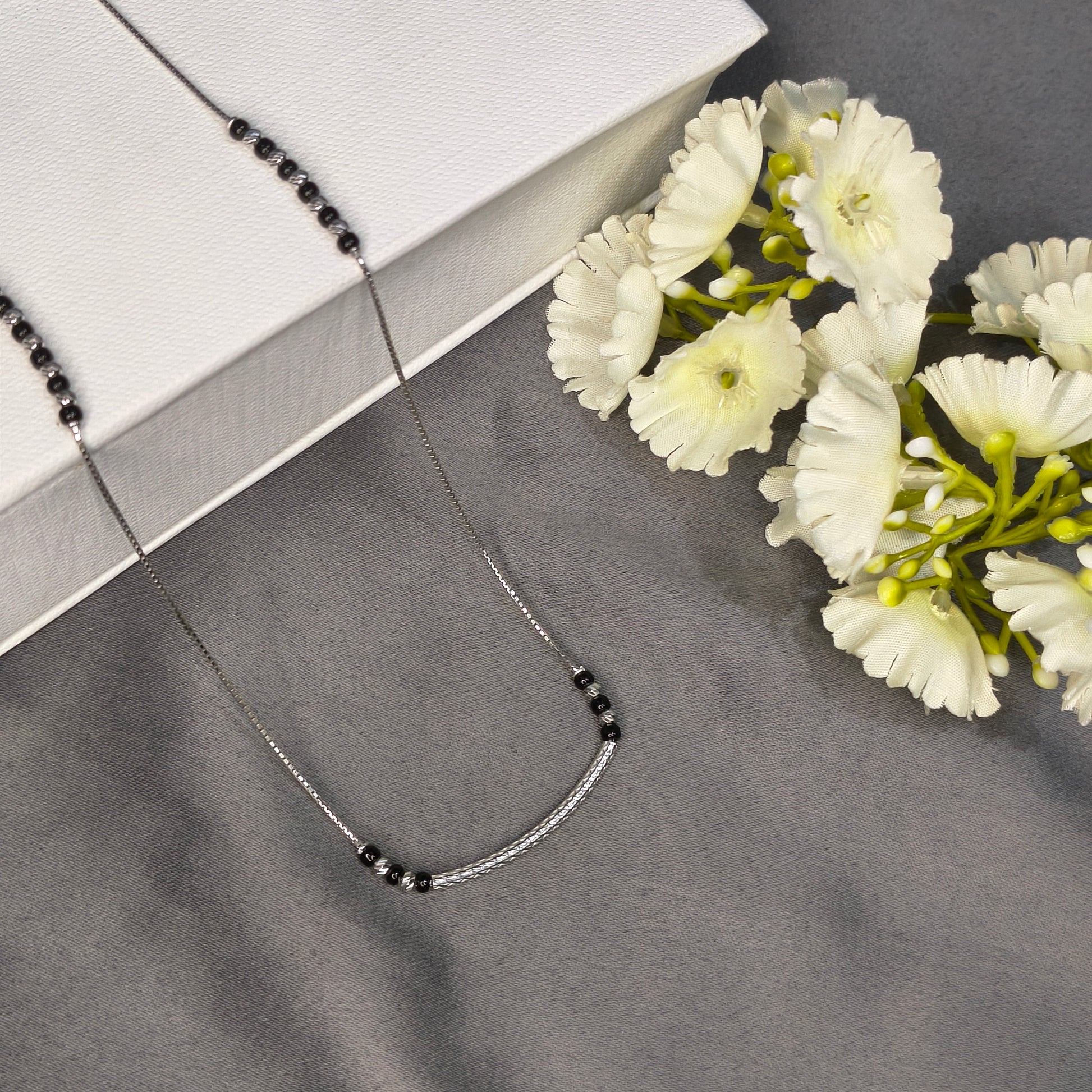 Necklace with black beads on a gray surface with white flowers