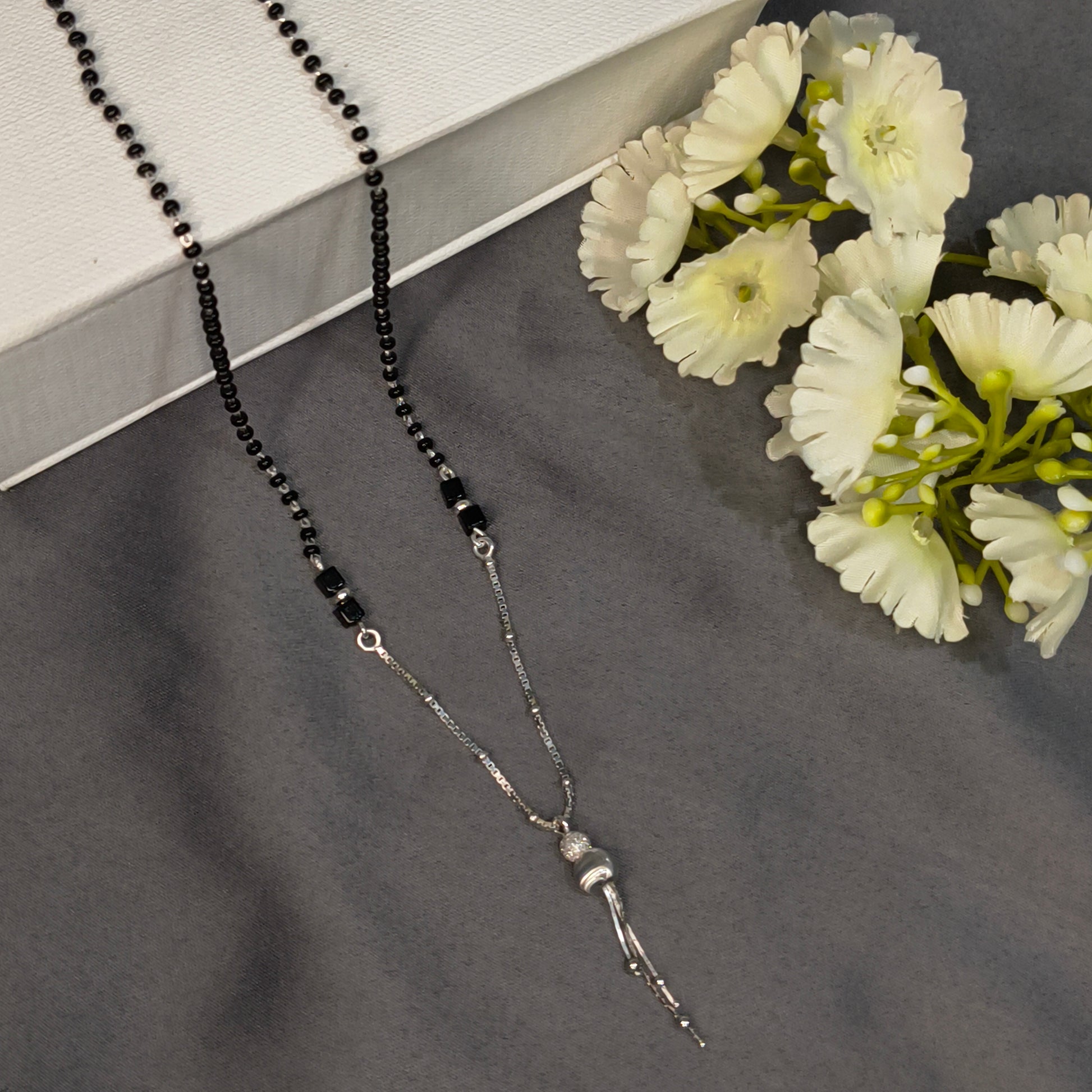 Black beaded necklace on a dark surface with white flowers
