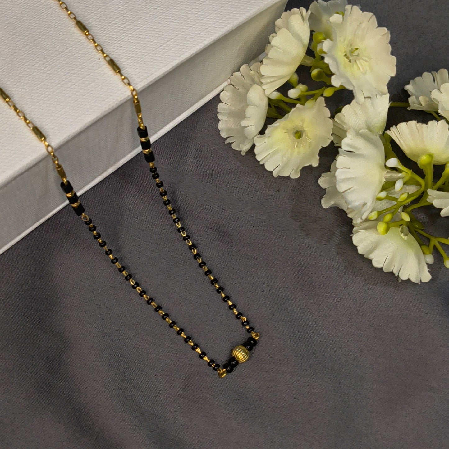 Necklace with black and gold beads on a gray surface with white flowers.