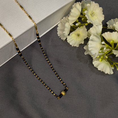 Necklace with black and gold beads on a gray surface with white flowers.