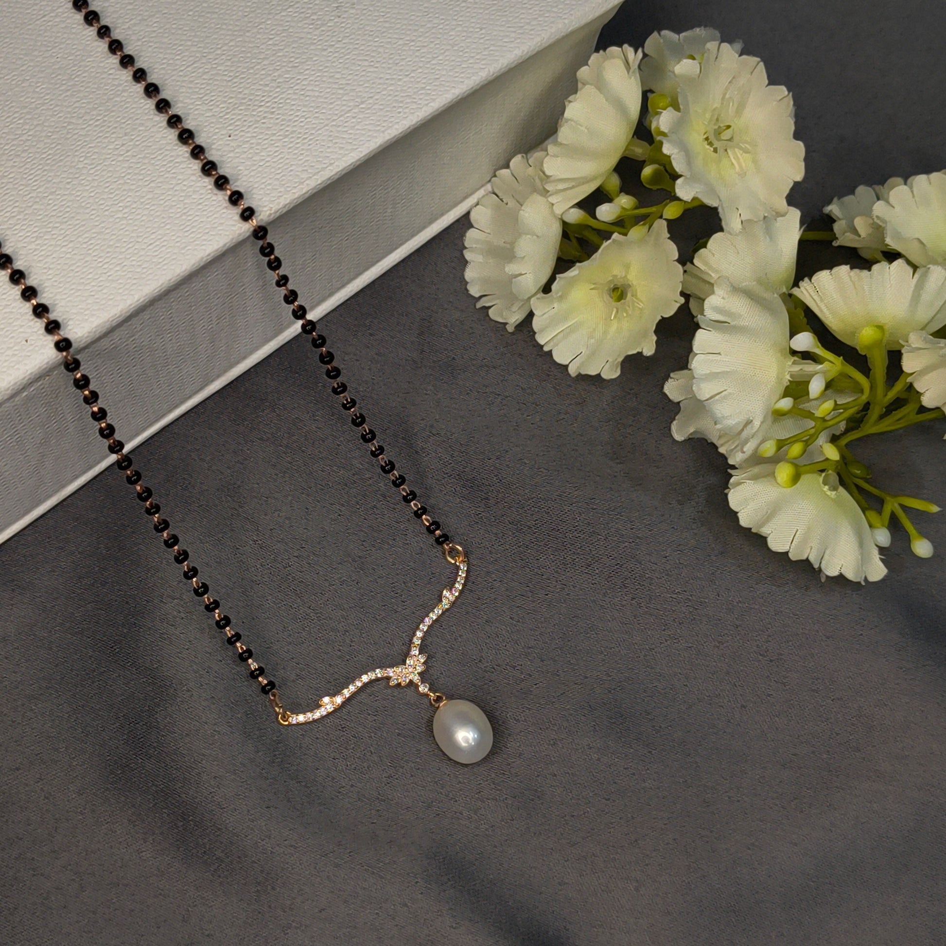 Necklace with a pearl pendant on a dark surface with white flowers