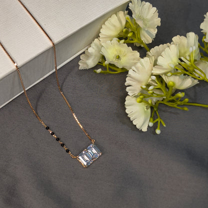Gold necklace with a rectangular pendant on a gray surface with white flowers.