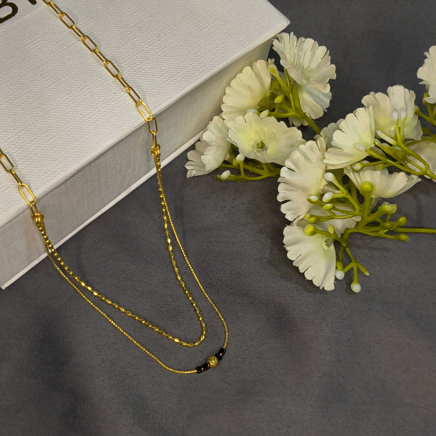 Gold chain necklace on a white box with white flowers on a gray background
