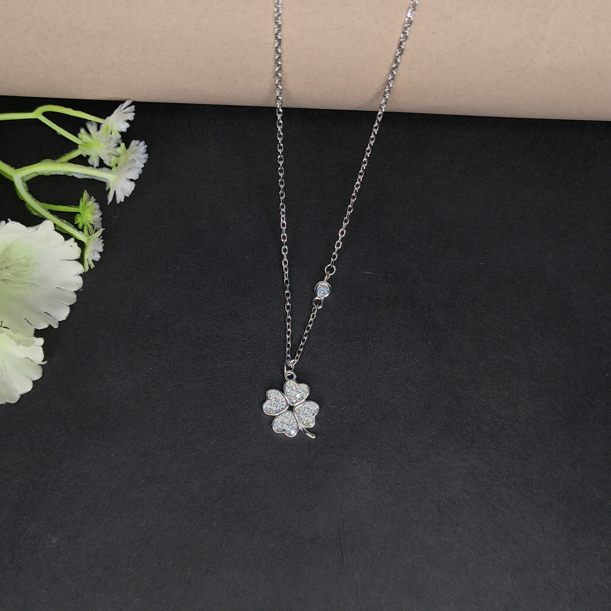 Silver necklace with a floral pendant on a dark surface with flowers.