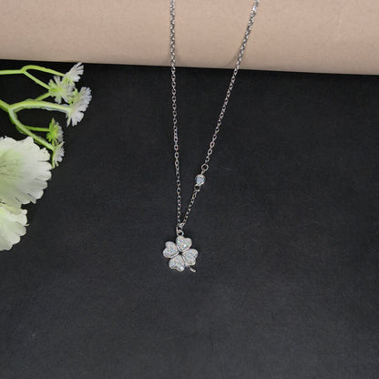 Silver necklace with a floral pendant on a dark surface with flowers.