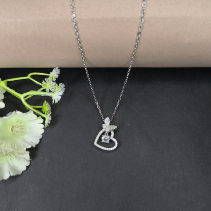 Silver necklace with a heart-shaped pendant on a dark surface with a white flower.