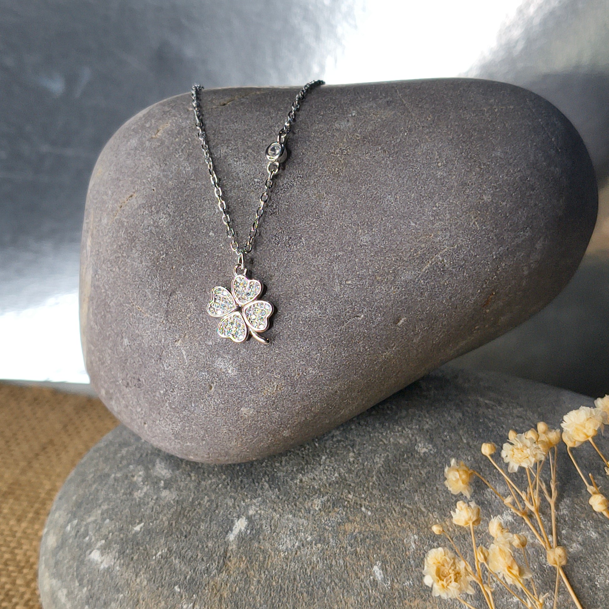 Silver four-leaf clover necklace on a gray stone with dried flowers in the background
