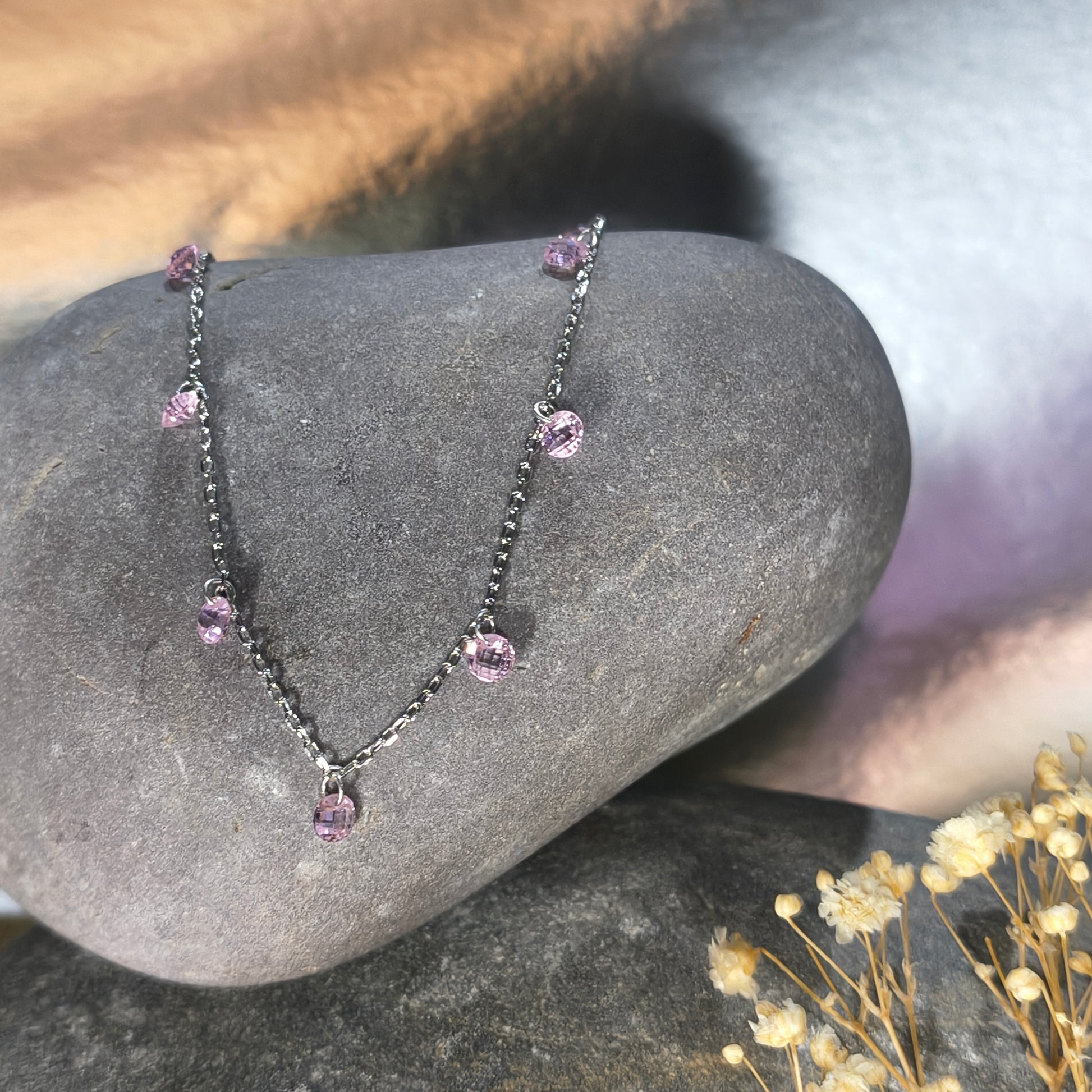 Silver chain bracelet with pink gemstones on a stone surface