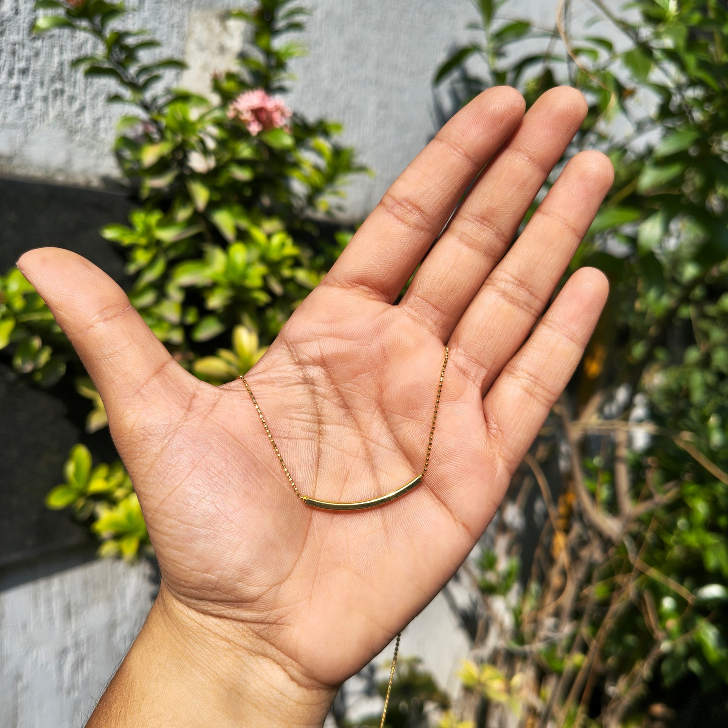 Hand wearing a gold chain with a blurred natural background