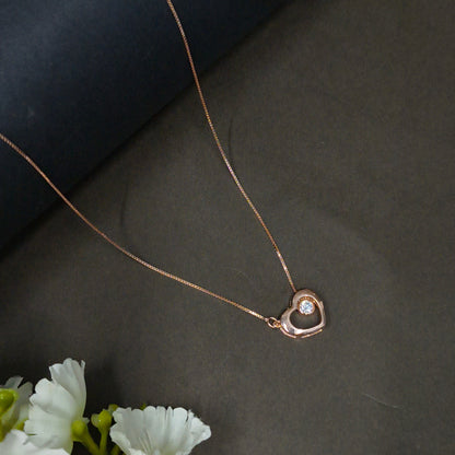 Rose gold necklace with a heart-shaped pendant on a dark background with white flowers.
