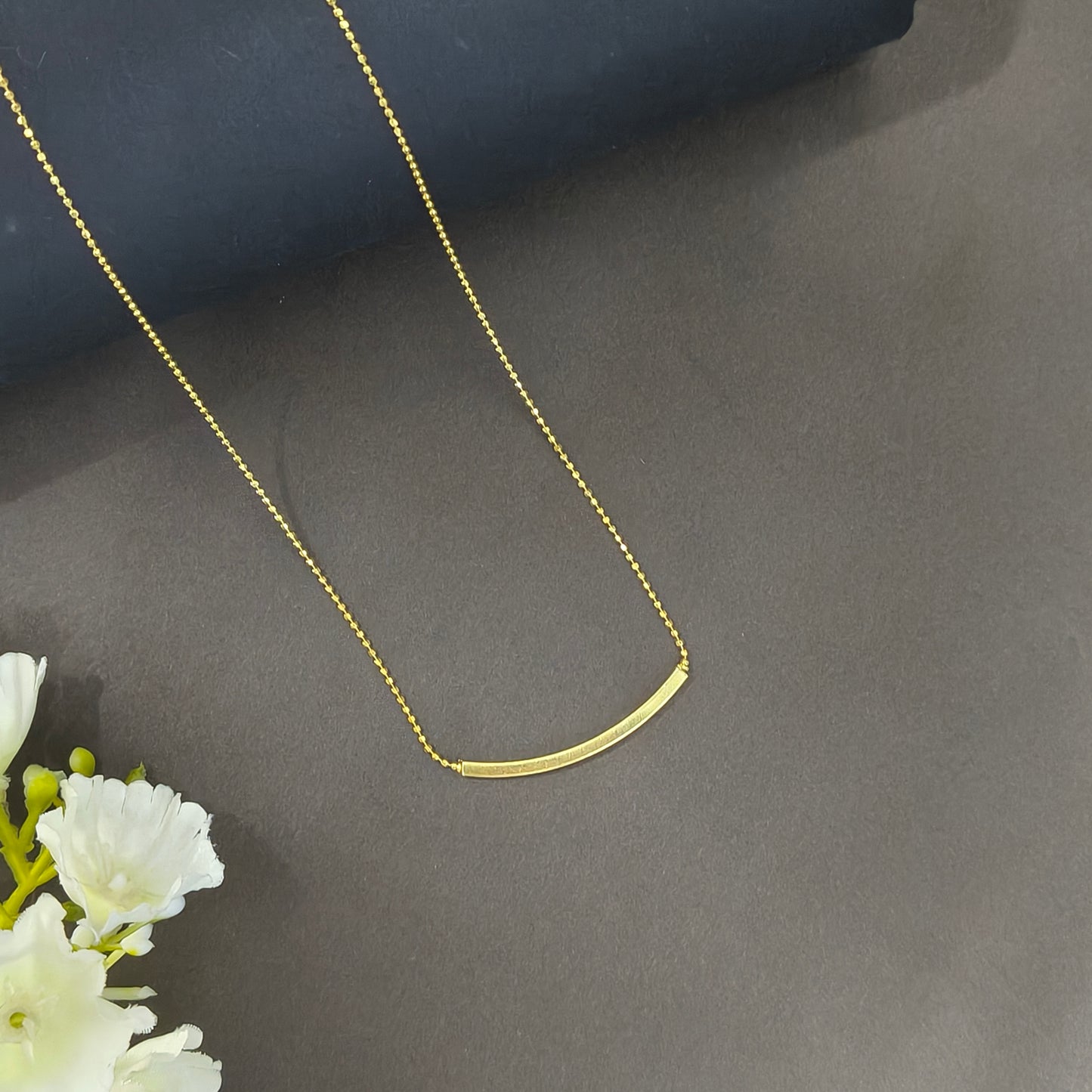 Gold necklace on a dark surface with white flowers