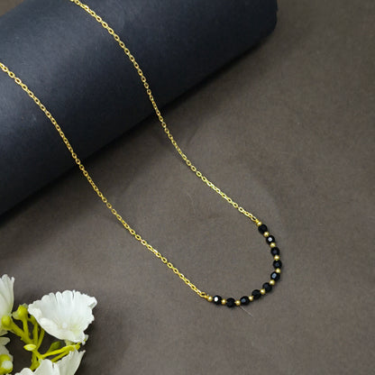 Gold chain necklace with black beads on a dark surface with white flowers.