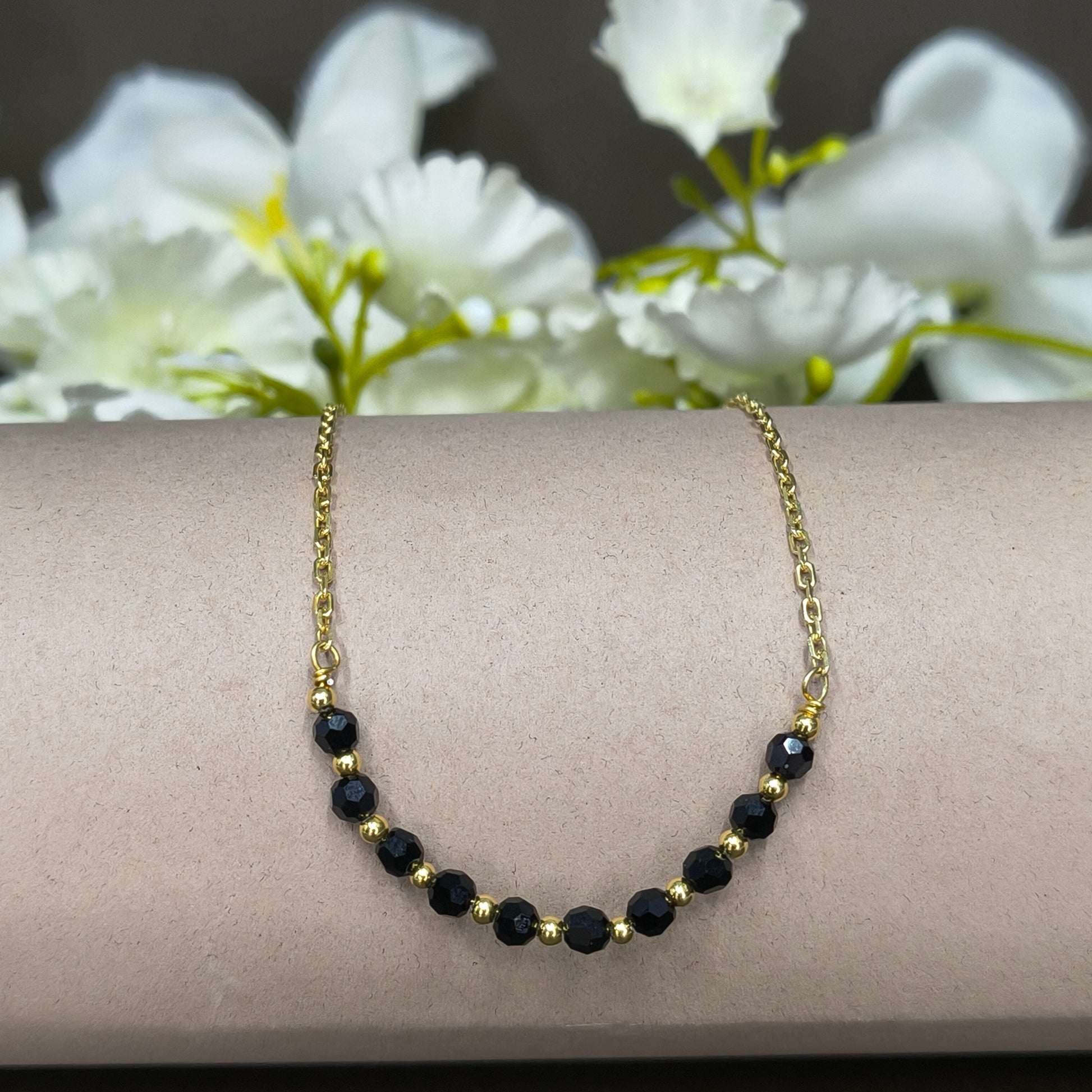 Gold bracelet with black beads on a wrist against a white flower background