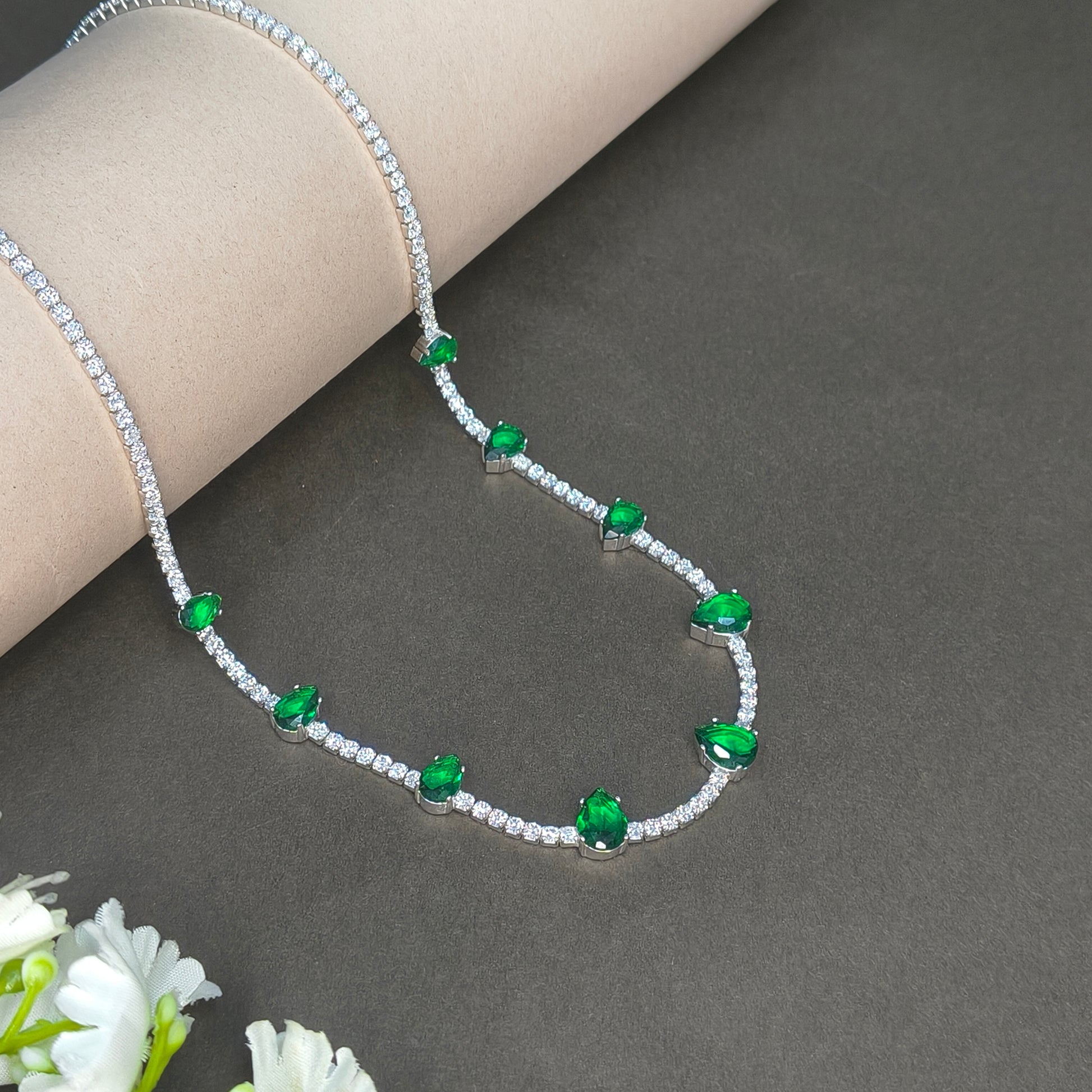 Silver necklace with green gemstones on a gray background